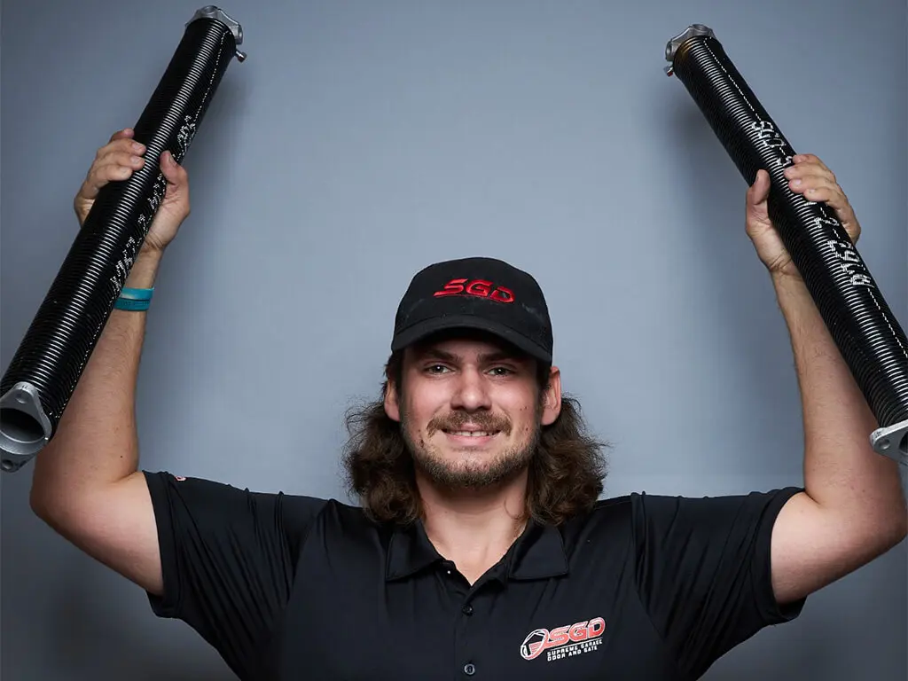 Professional Supreme Garage Door Repair technician holding two heavy-duty replacement torsion springs in Dallas